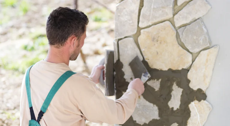 Worker applying mortar between irregular stone wall sections