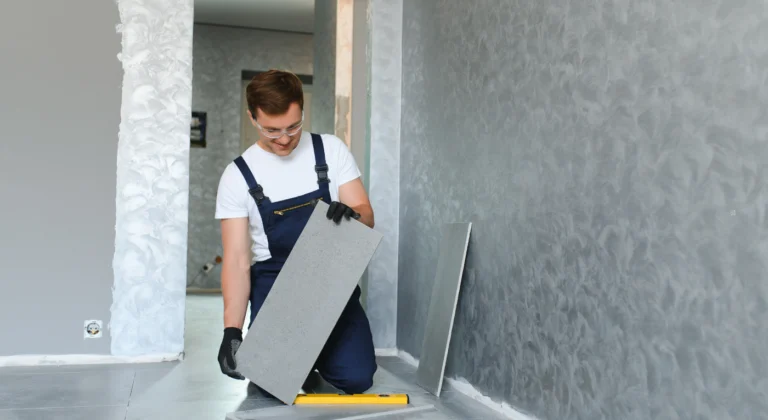 Worker positioning a large gray tile beside a tiled wall