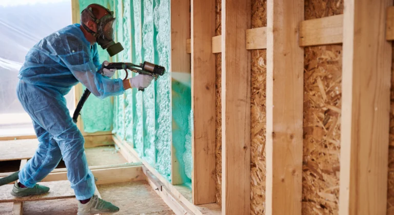 Worker applying spray foam insulation between exposed wall studs